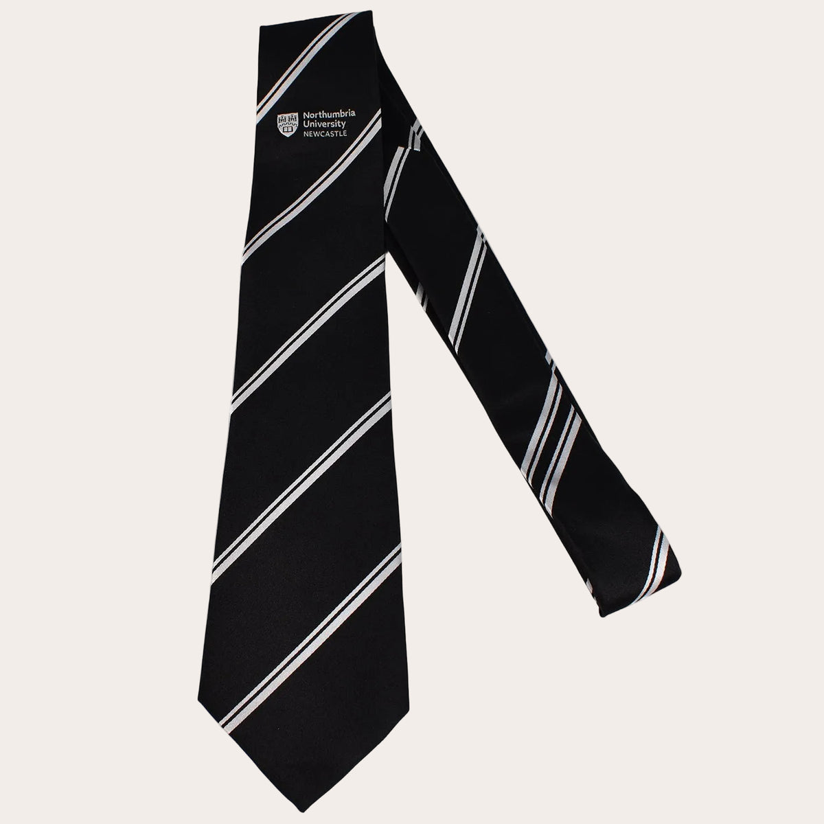 A black necktie with diagonal white and silver stripes, featuring the University of Manchester mark on the upper left, displayed against a solid white background.