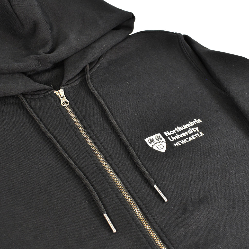 A close-up of a black zip-up hoodie with a white embroidered logo for Northumbria University on the chest. The hoodie features black drawstrings with silver metal tips and a gold-toned zipper.